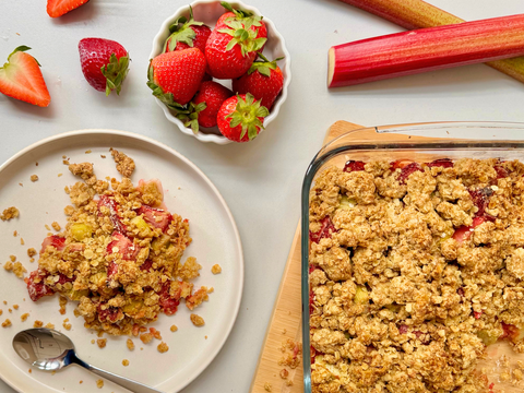 Veganer Erdbeer-Rhabarber Crumble mit knusprigen Streuseln in einer Auflaufform, serviert mit cremiger Vanillesoße.