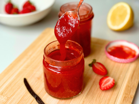 Selbstgemachte Erdbeer-Vanille-Konfitüre in einem Glas mit frischen Erdbeeren und Vanilleschoten auf einem Holztisch.