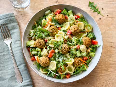 Bunter Nudelsalat mit Ohrnudeln, Linsenbällchen, Paprika, Gurke, Möhren, Rucola und Lauchzwiebeln in einer großen Schüssel.