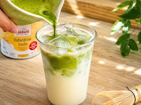 Cremiger Vanille Matcha Latte mit Haferdrink und Eiswürfeln in einem Glas, geschichtet mit grünem Matcha und pflanzlichem Vanilledrink.
