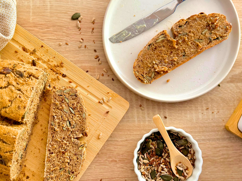 Frisch gebackenes Vollkorn-Sauerteigbrot mit Kürbis- und Sonnenblumenkernen auf einem Holzbrett.