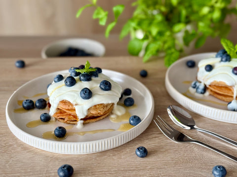 Fluffige vegane Pancakes mit Blaubeeren, pflanzlichem Joghurt und Agavendicksaft auf einem Teller angerichtet.